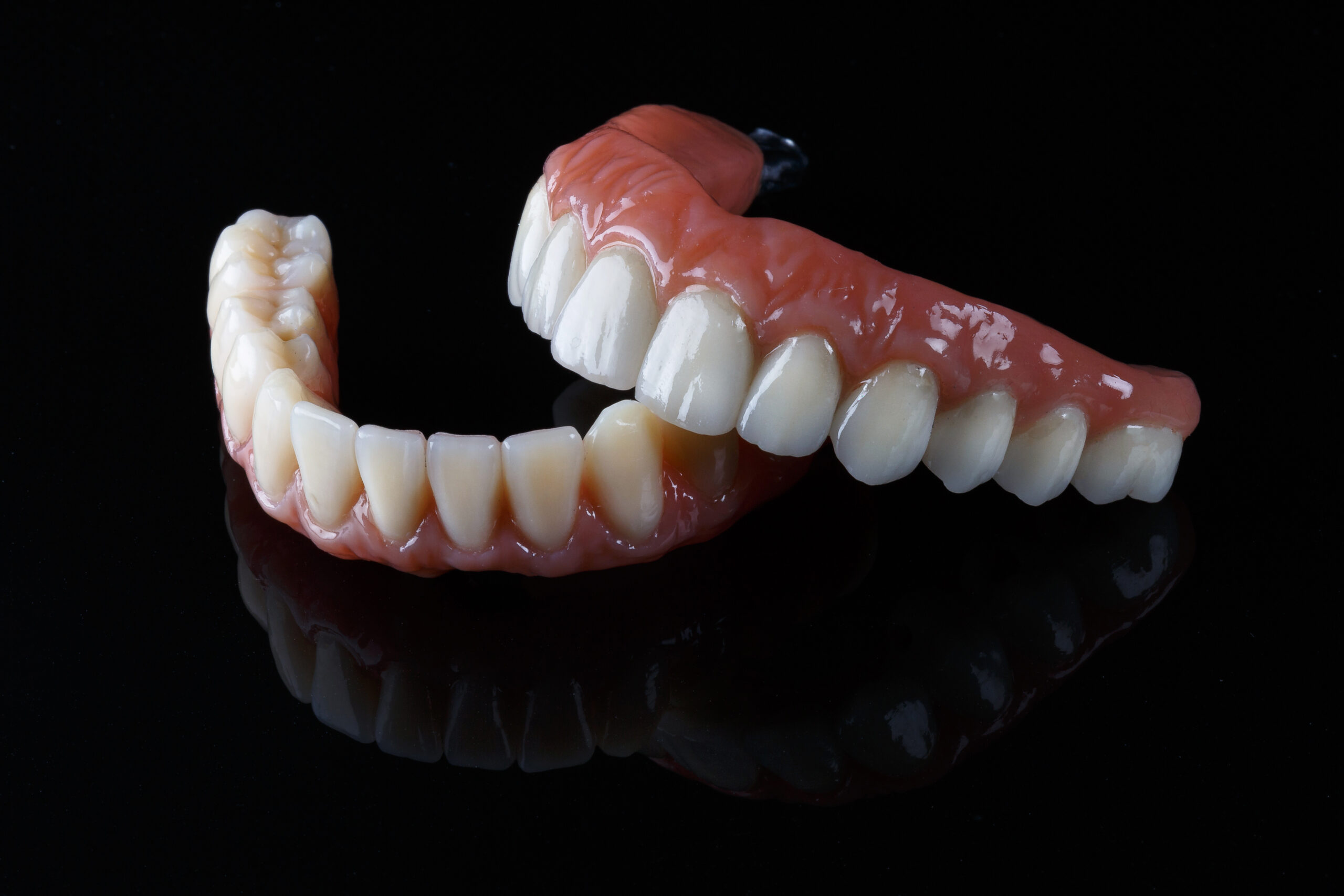 ceramic prosthesis with artificial gums, upper and lower jaw on black glass.